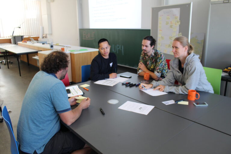 Four PUSH-IT members are sitting around a table discussing.